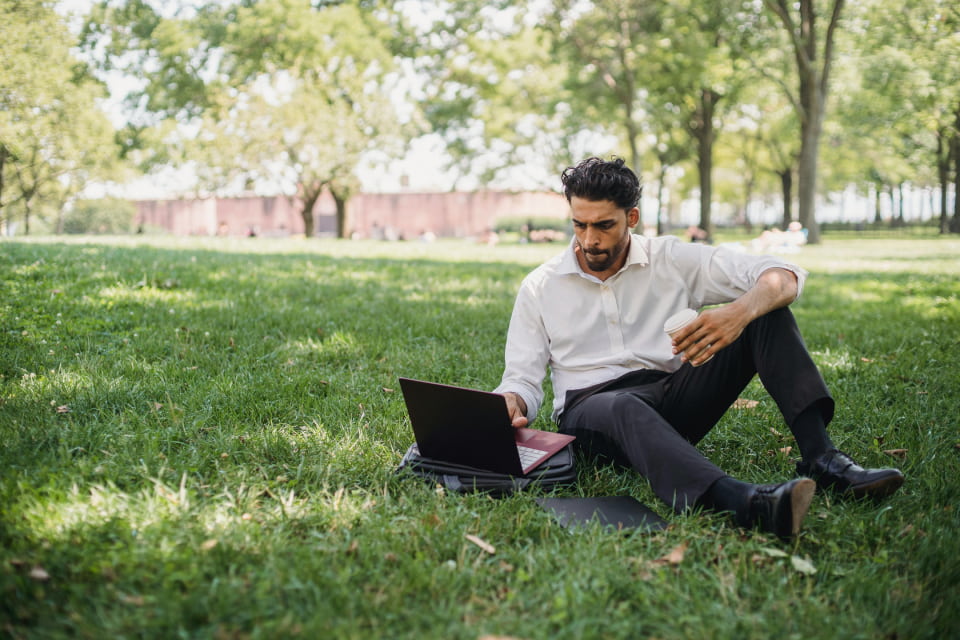 man sitting on grass looking as laptop
